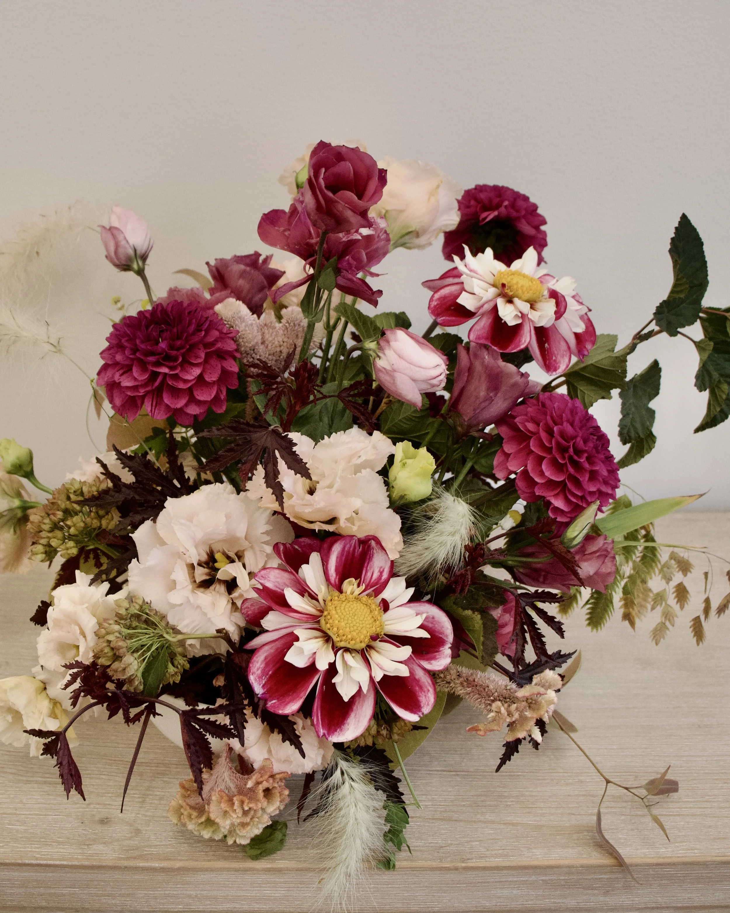 Arrangement of pink, white, and maroon flowers with green leaves on a light wooden surface