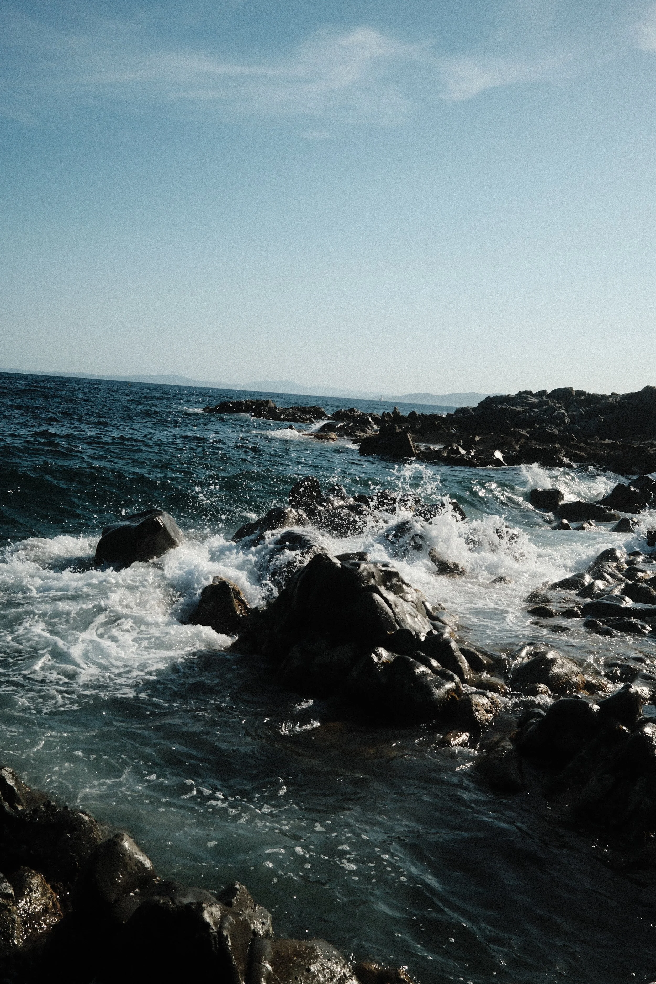 Rocky shoreline with ocean waves crashing on the rocks under a clear sky