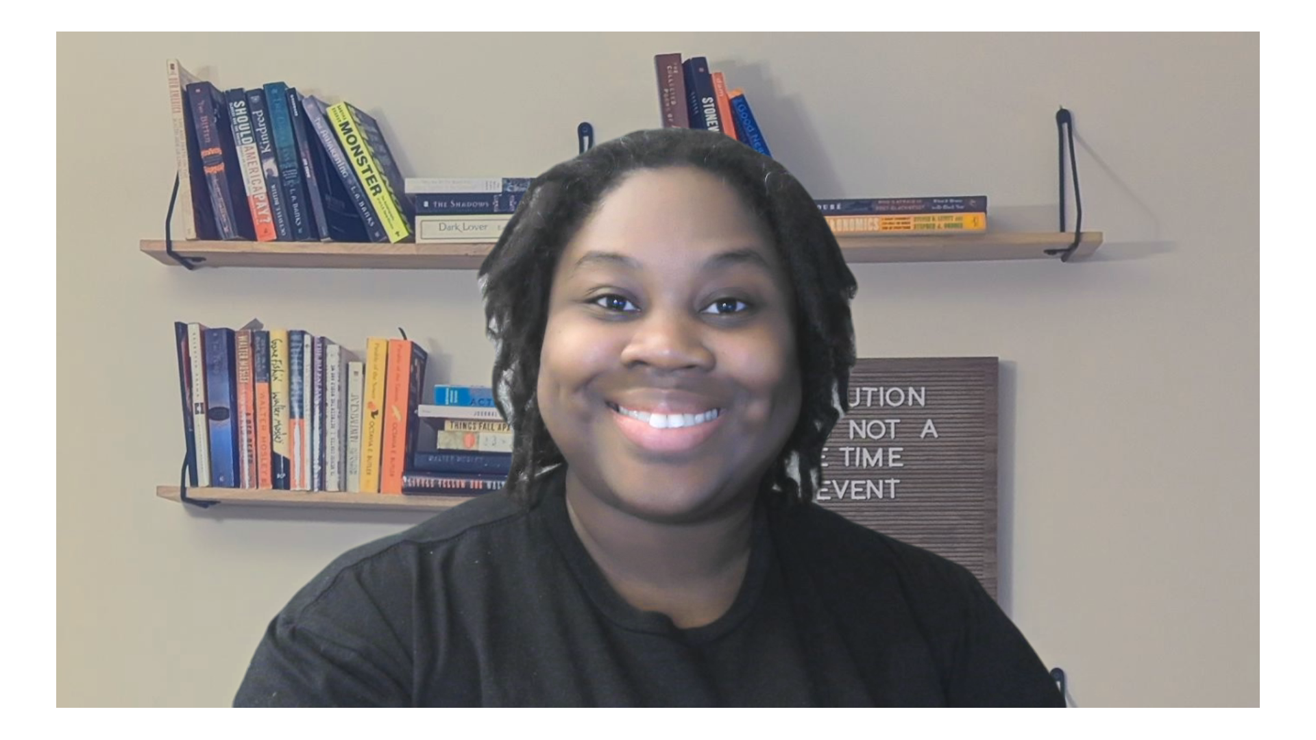 Smiling woman with dreadlocks in front of a bookshelf filled with colorful books, and a letter board with the words 'CATION' and 'NOT A TIME EVENT' visible.