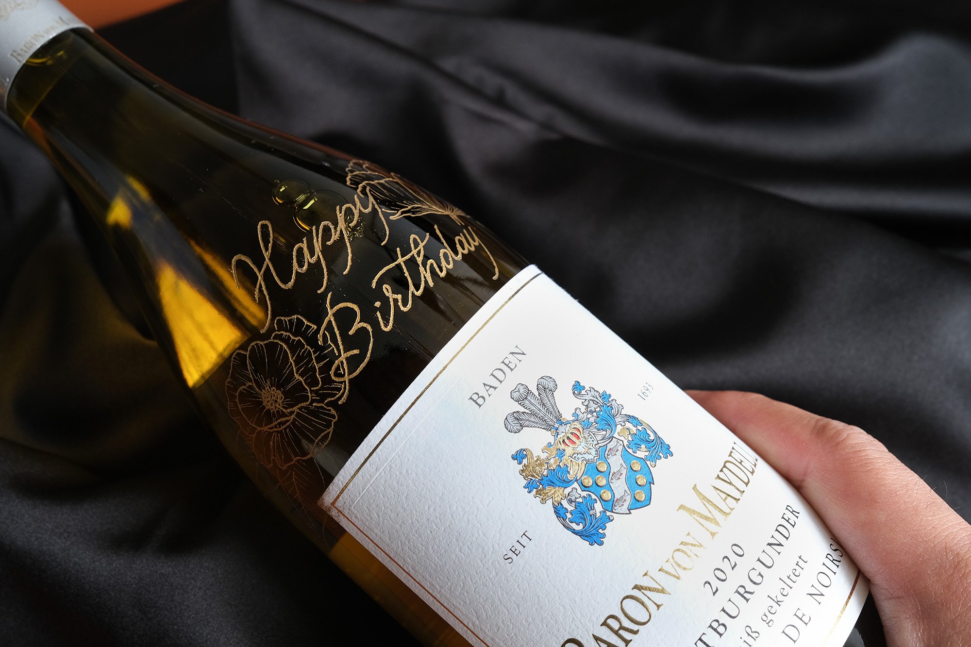 Weinflasche mit "Happy Birthday" Gravur, Baden Etikett, Gewölbe auf einem Stoffhintergrund.