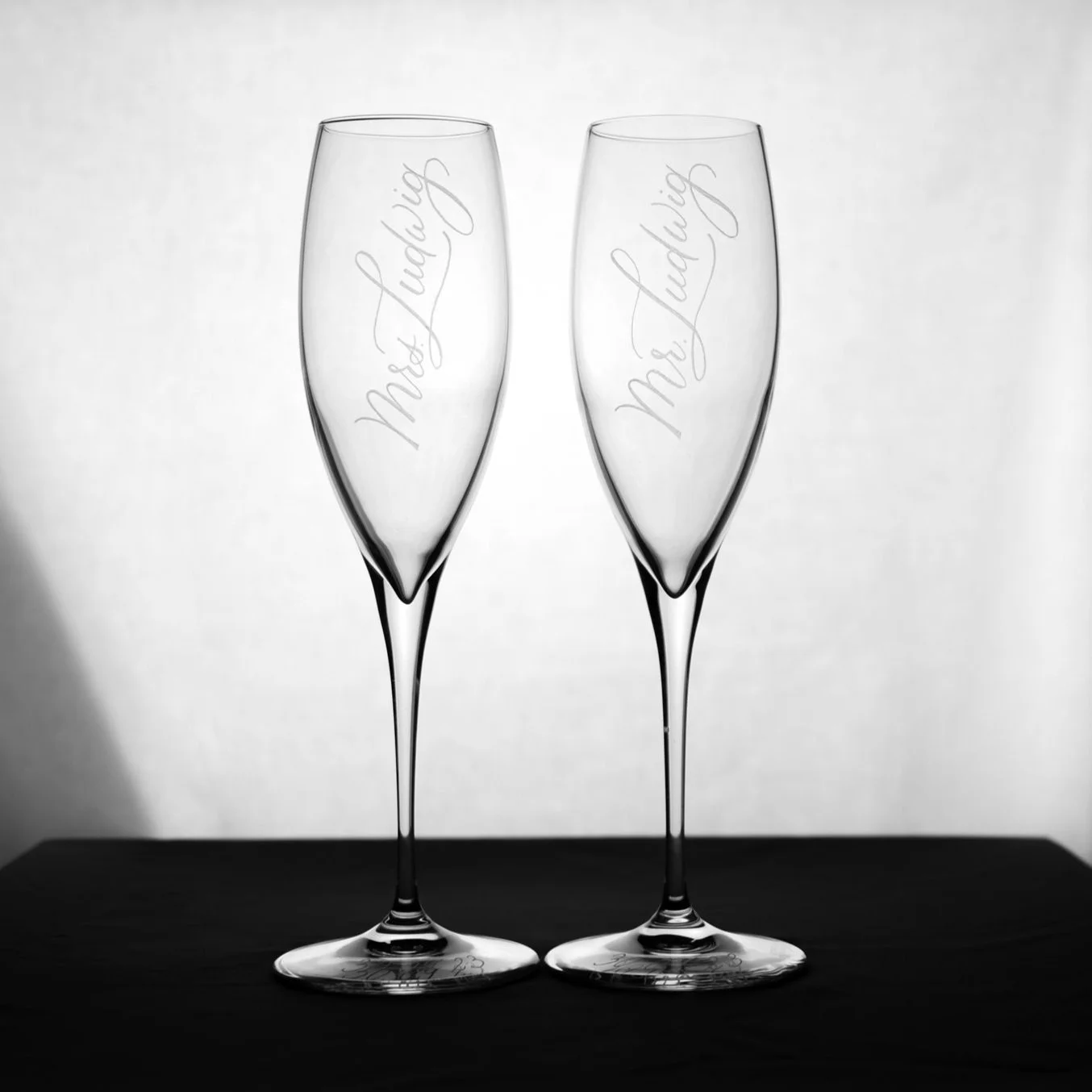Zwei leere Champagnergläser mit Gravuren auf einem schwarzen Tisch.