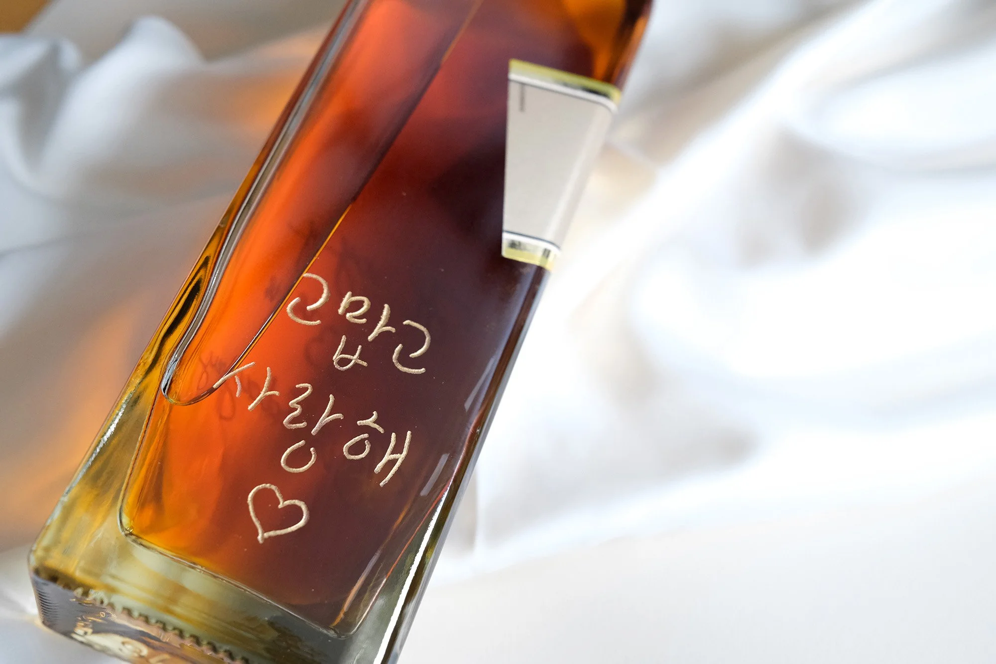 Nahaufnahme einer Glasflasche mit brauner Flüssigkeit und koreanischer Aufschrift auf einem weißen Hintergrund.