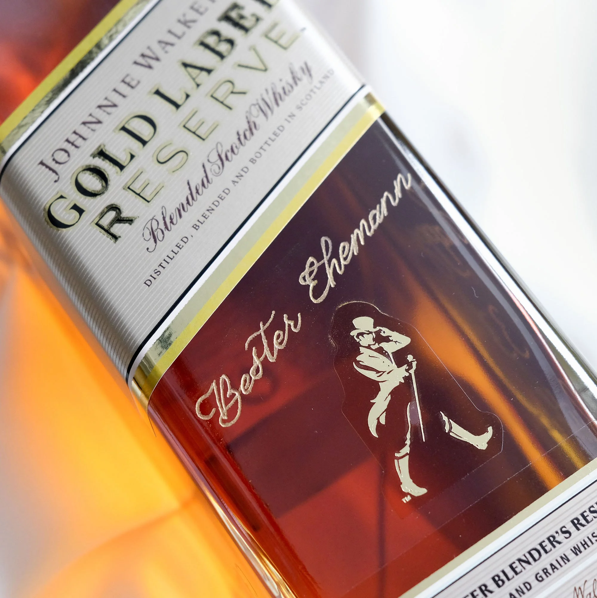 Nahaufnahme einer Whiskyflasche Johnnie Walker Gold Label Reserve mit der Aufschrift "Bester Ehemann" und dem ikonischen Gehmann-Logo.