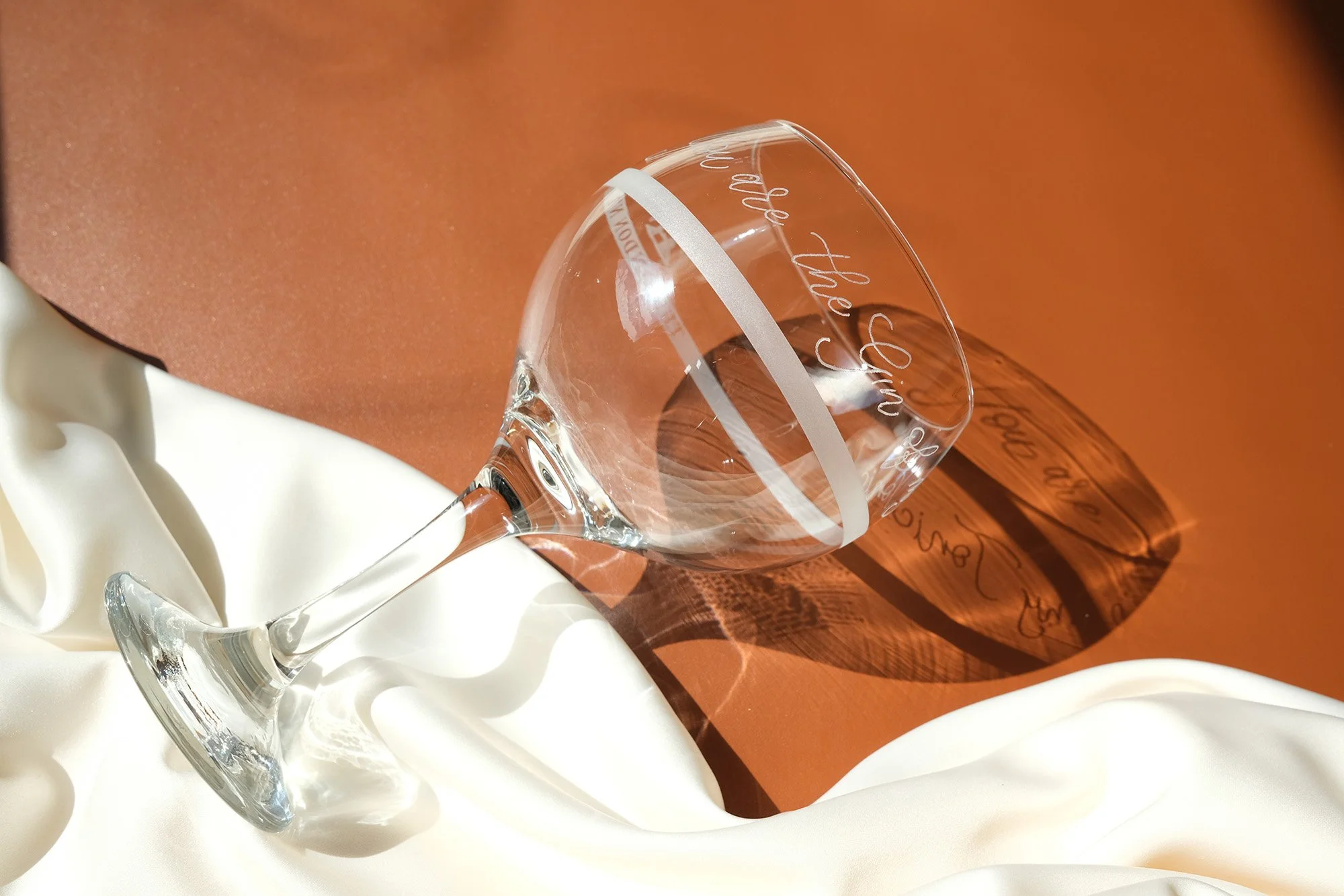 Weinglas auf einem weißen Tuch liegend, mit Gravur auf der Glasoberfläche, auf einem braunen Hintergrund.