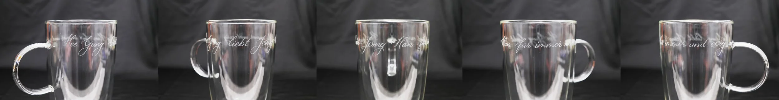 Fünf Glastassen mit graviertem Schriftzug auf schwarzem Hintergrund.