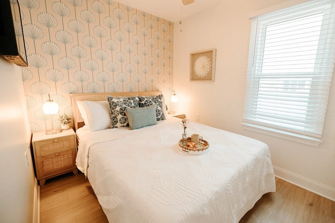 Coastal bedroom with patterned wallpaper, neutral bedding, wood nightstands, and blue accent pillows