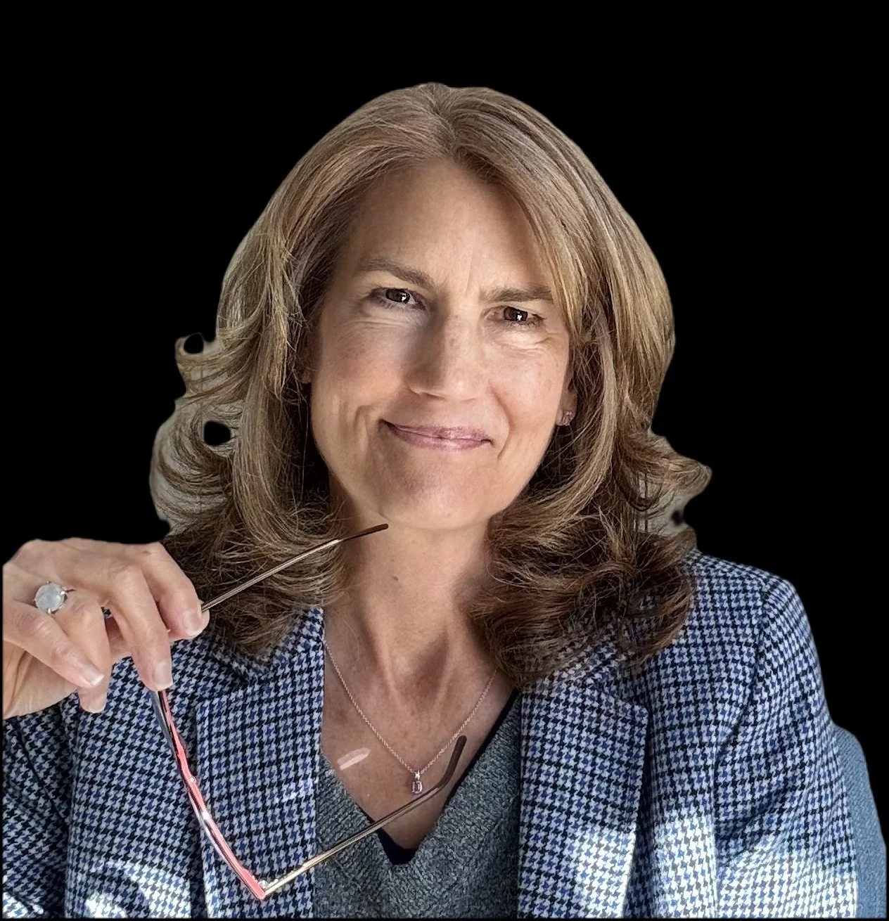 A woman with blonde, wavy hair, wearing a checkered blazer, holding eyeglasses, and smiling at the camera against a black background.