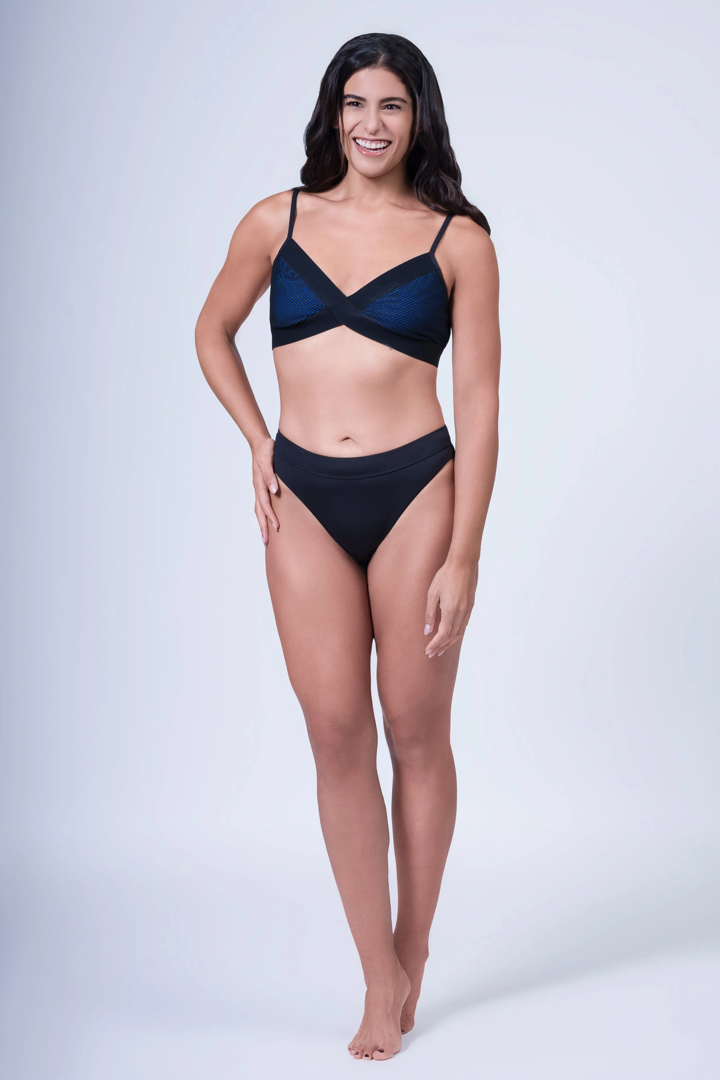 A woman standing in a swimsuit, smiling, against a plain light background.