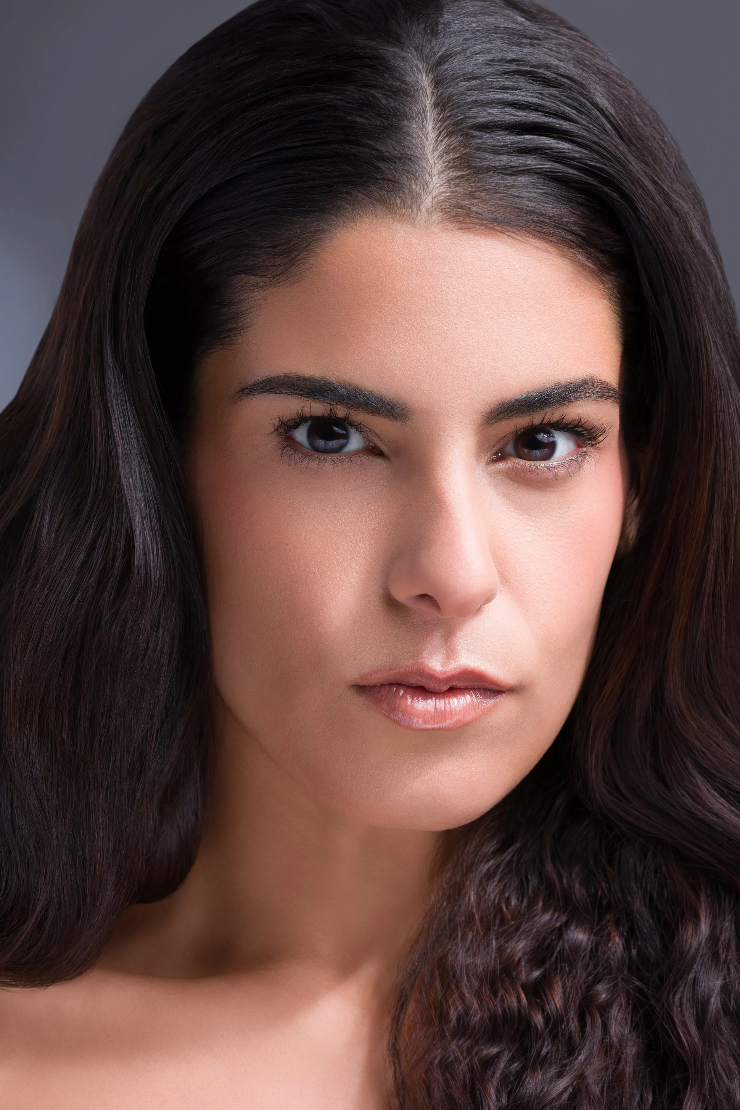 Close-up portrait of a woman with dark, wavy hair, one eye closed, looking directly at the camera.