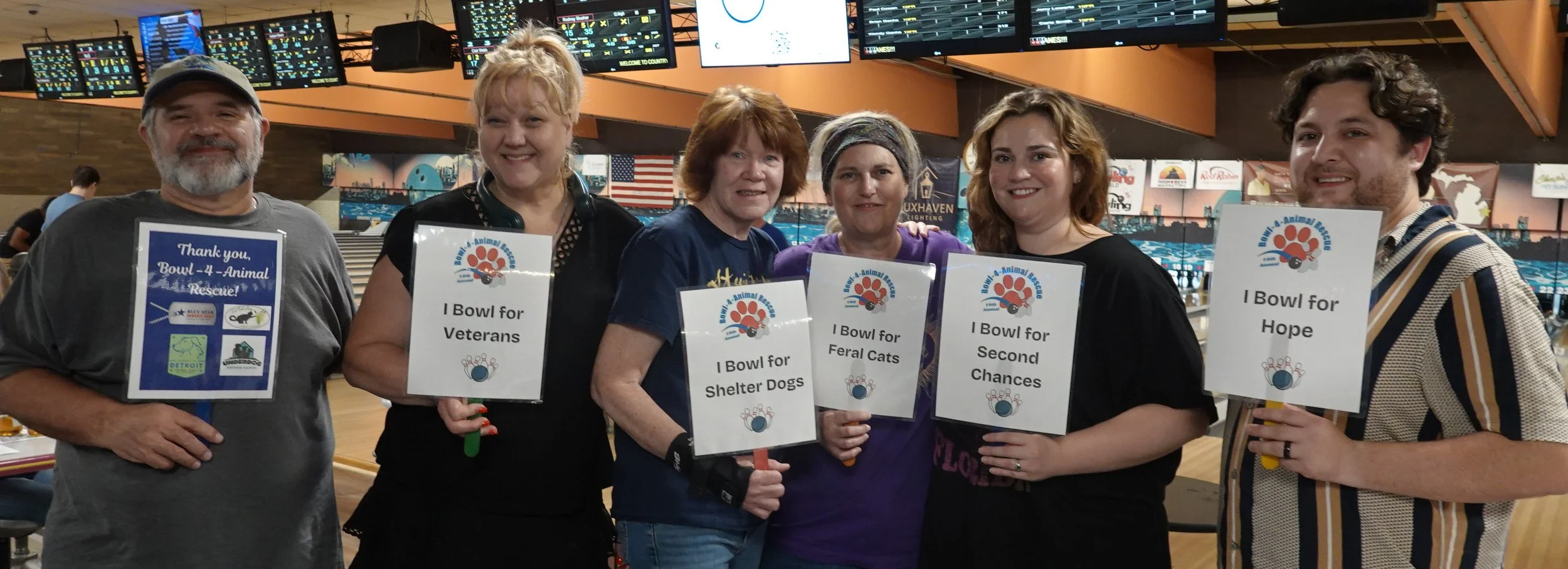 A bowling team holdingup signs showing why they bowl for veterans, for shelter dogs, for feral cats, for second chances, and for hope.