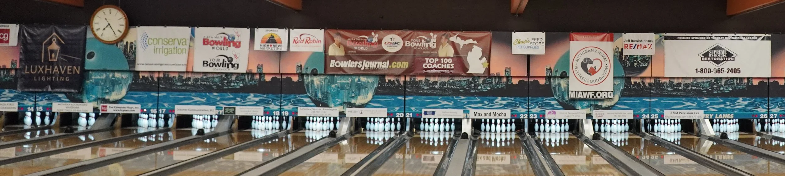 A row of bowling lanes with banners featuring the lane sponsors above each one.