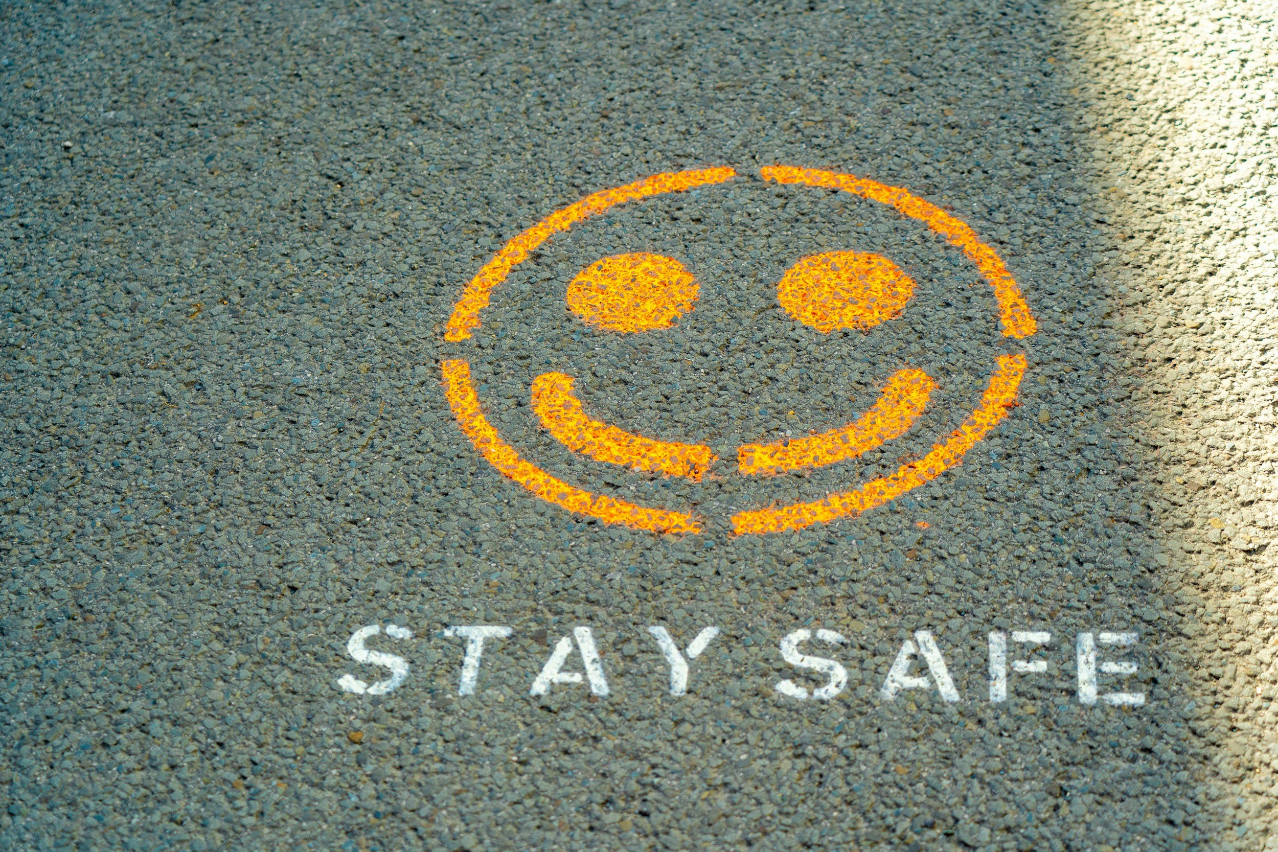 Yellow painted smiley face on street with the words 'STAY SAFE' written underneath.