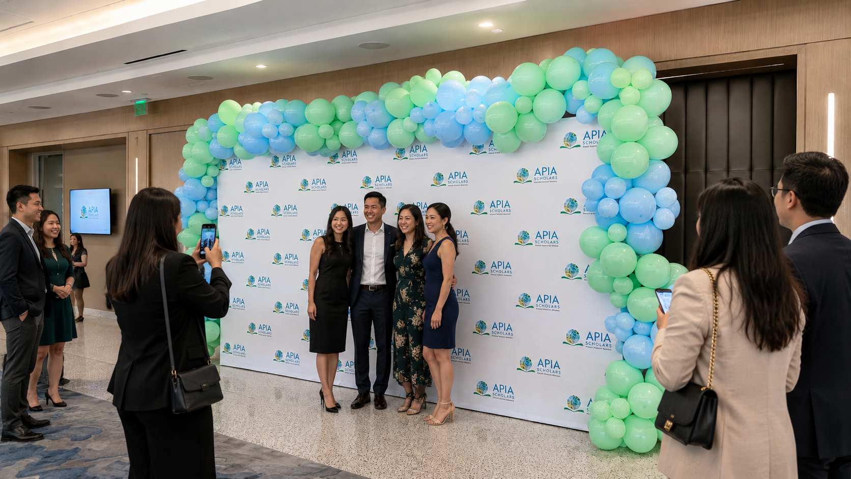 Guests posing in front of a custom branded step and repeat backdrop with organic balloon garland at a corporate event in Dallas.