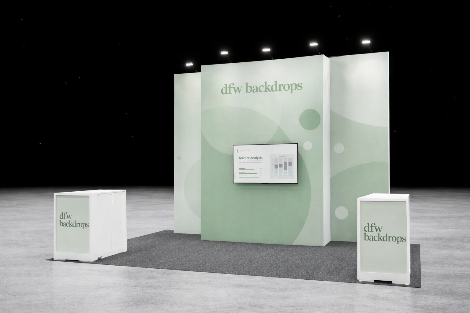 Trade show display booth with green-themed backdrop displaying 'dfw backdrops', a monitor showing market analysis, and two white counters labeled 'dfw backdrops' on an empty exhibition floor.