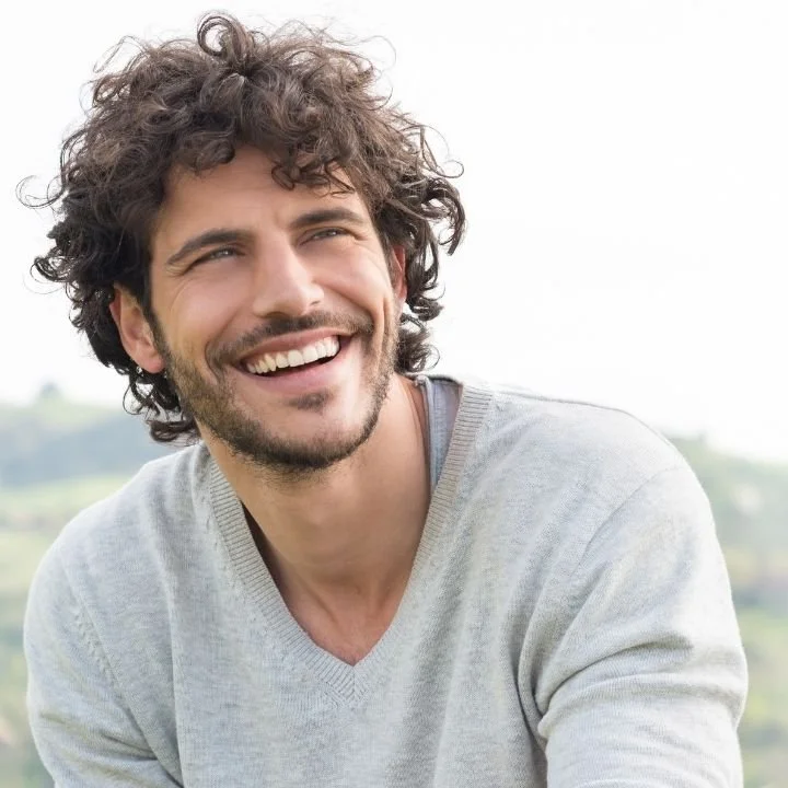 Man smiles broadly while looking off to the side outdoors.