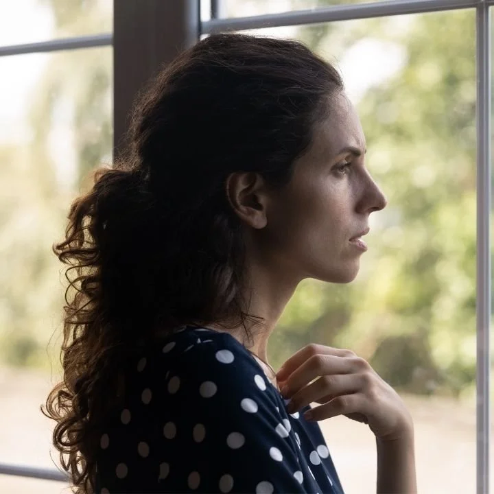 Woman looking out window with reflective expression.