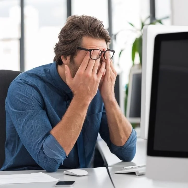 Man rubbing his eyes at a desk while experiencing difficulty maintaining attention.