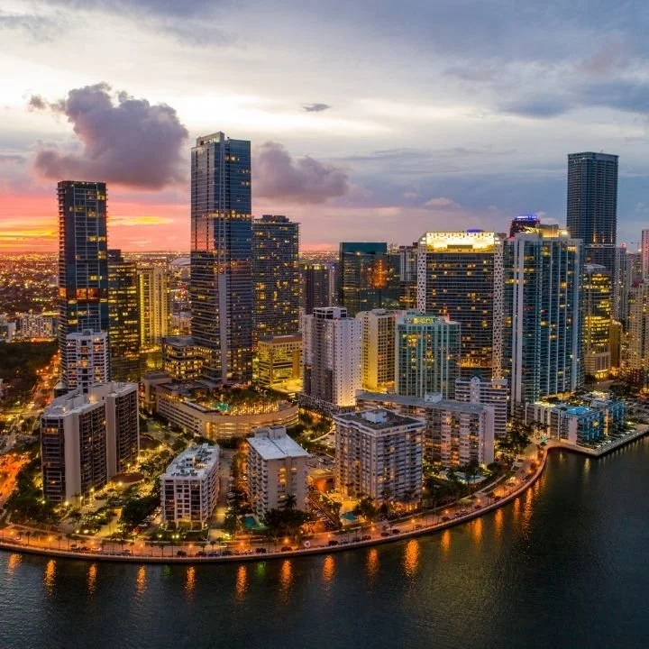 Miami skyline at sunset with high-rise buildings glowing along the waterfront.