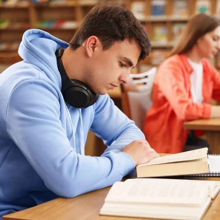 Teenager sits quietly with arms folded, reading a book with a serious, inward-focused expression.