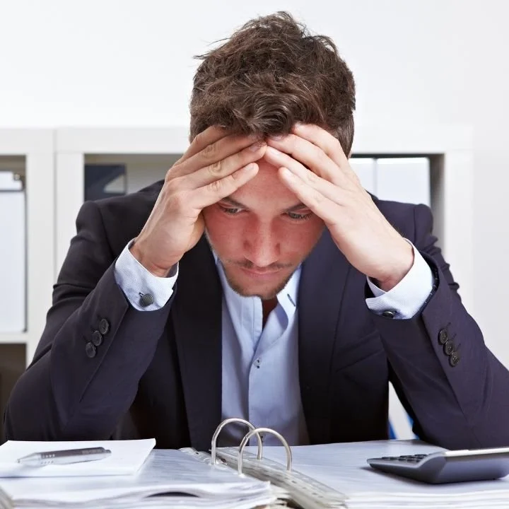 Man holding his head while reviewing paperwork, appearing overwhelmed and mentally drained.