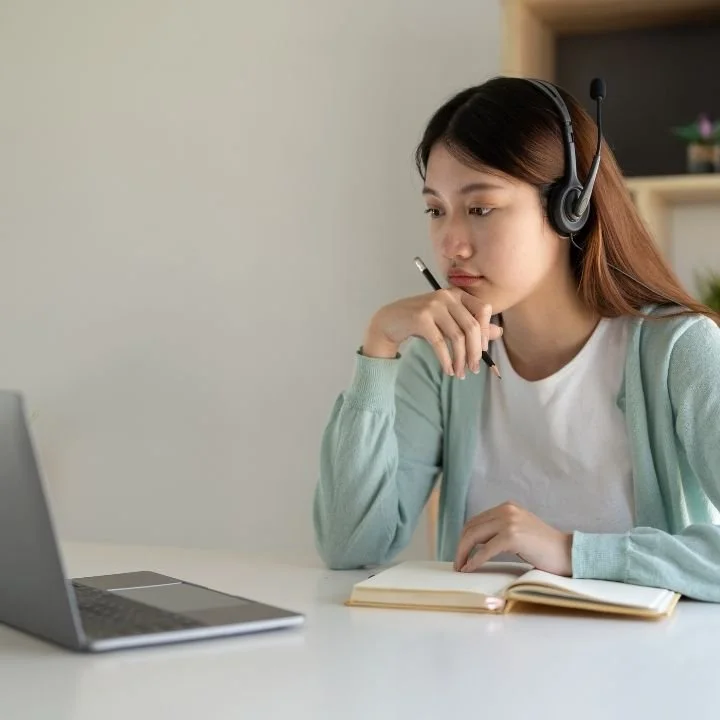 Woman rests her chin on her hand and smiles slightly while listening to a therapist during an online session.