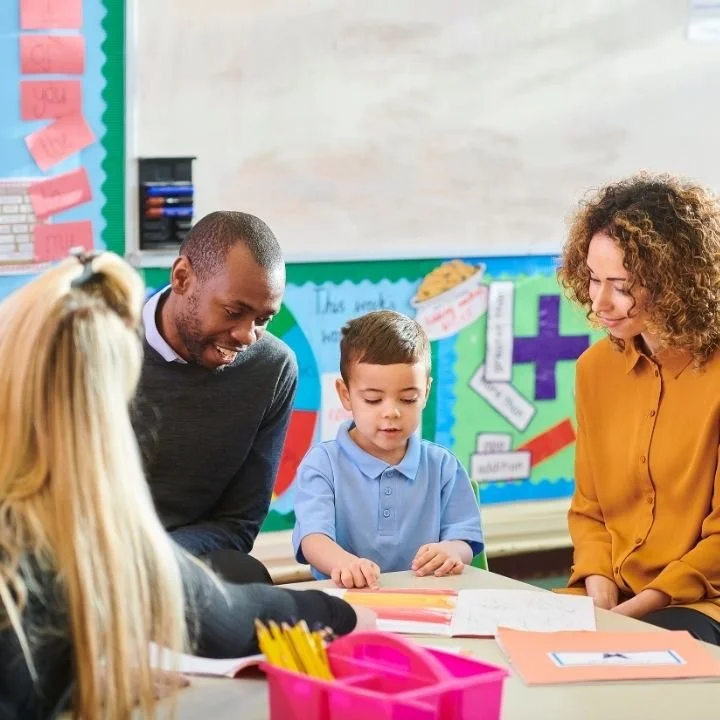 Teacher and parents helping a young student complete classroom learning activities.