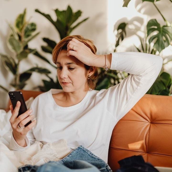 Woman sitting on couch looking at phone with concerned expression.