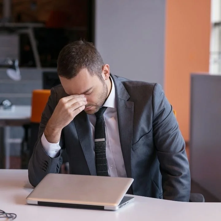 Man in suit holding his face while sitting at desk.