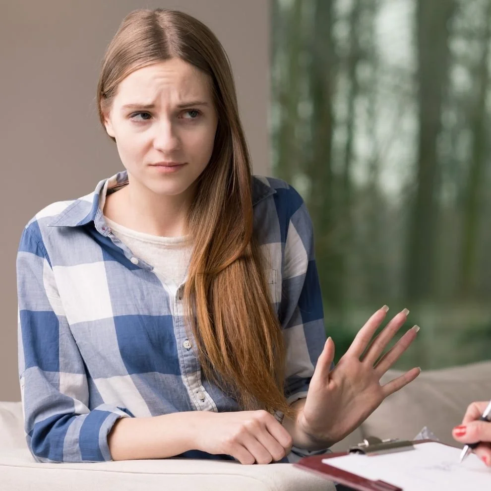 Woman raising hand with uncertain expression during discussion.
