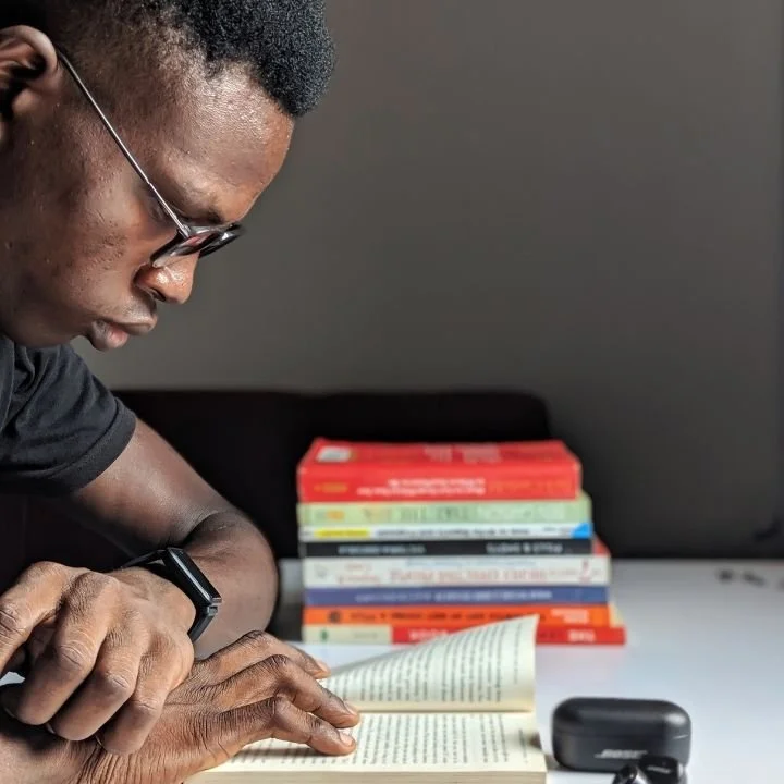 Man wearing glasses reading a book beside stack of colorful books