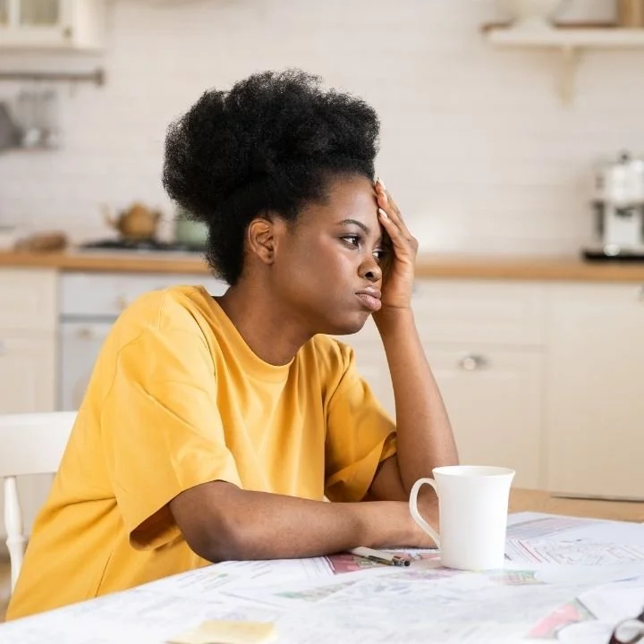 Woman resting her head on her hand and looking concerned while reviewing paperwork spread across a kitchen table.