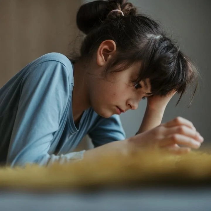 Teen leaning over book with frustrated expression while studying.