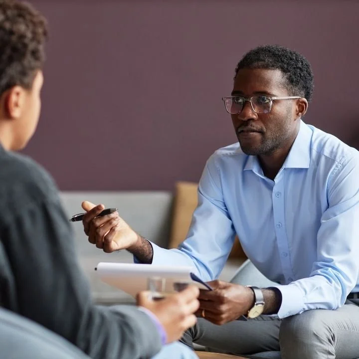 Male therapist holding pen and clipboard while talking to a teen boy client