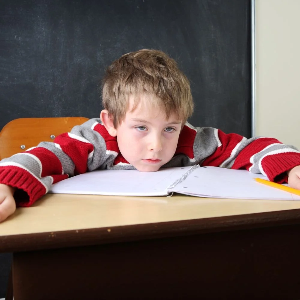 Tired child with ADHD slumped over desk with notebook