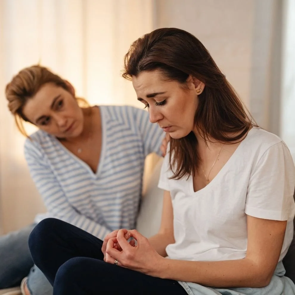 Two women sitting together, one offering emotional support during a difficult conversation.