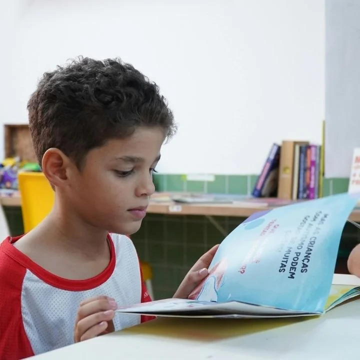 Young boy sitting at table reading a colorful illustrated children’s book