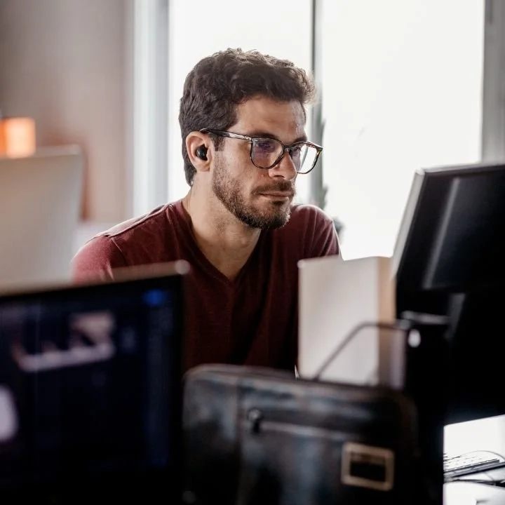 Man leans forward at his desk, focused on a computer screen with a serious expression.