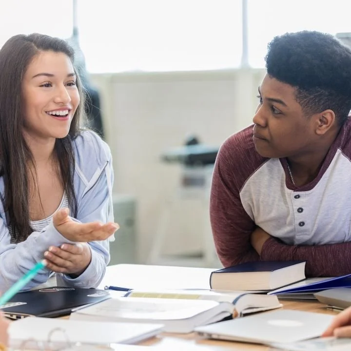 Teenagers talking at table, practicing communication during group discussion together.