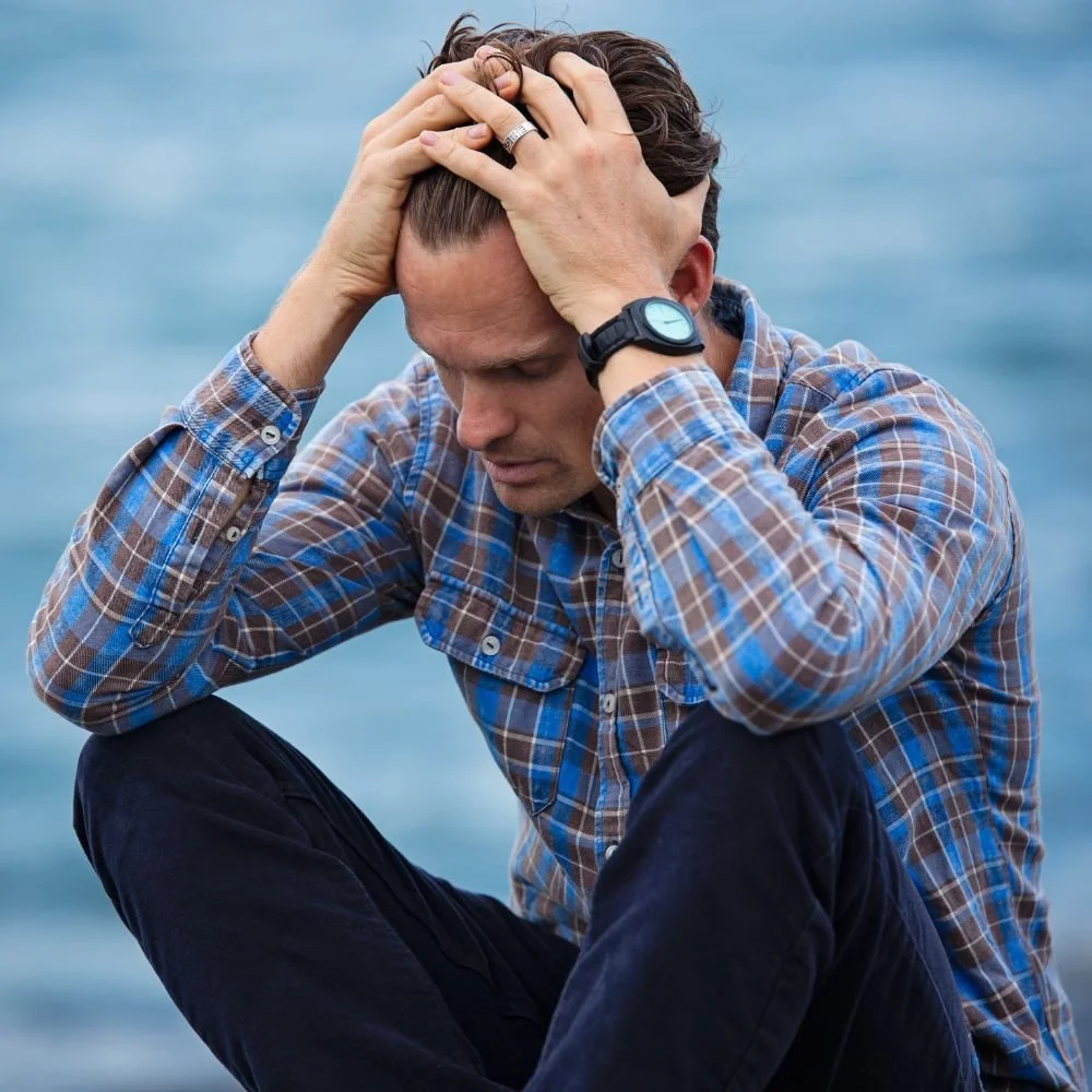 Man sitting outdoors holding head in frustration
