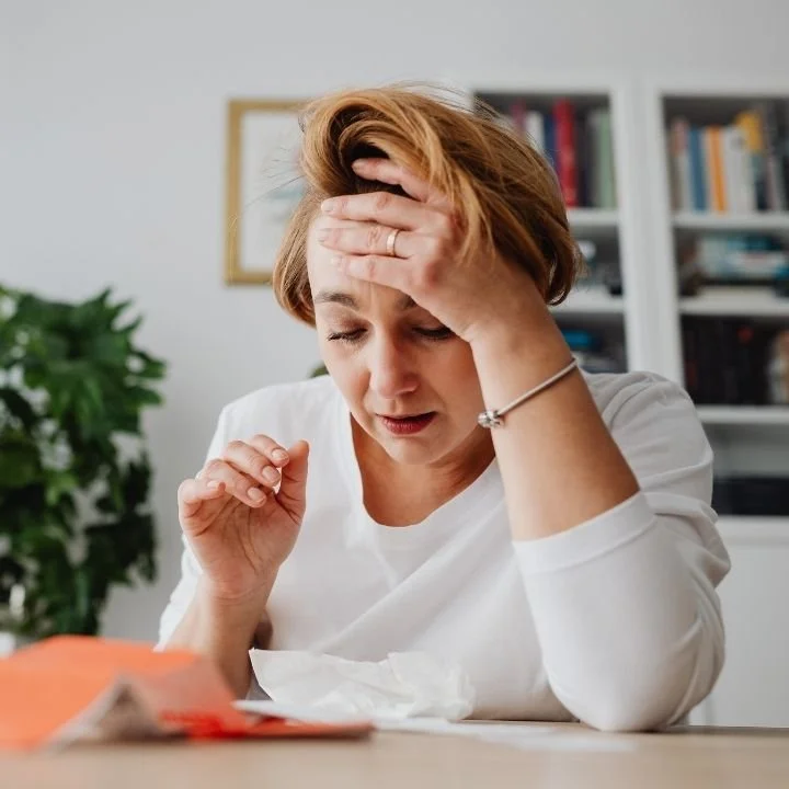 Adult woman holding head while reading, appearing overwhelmed.