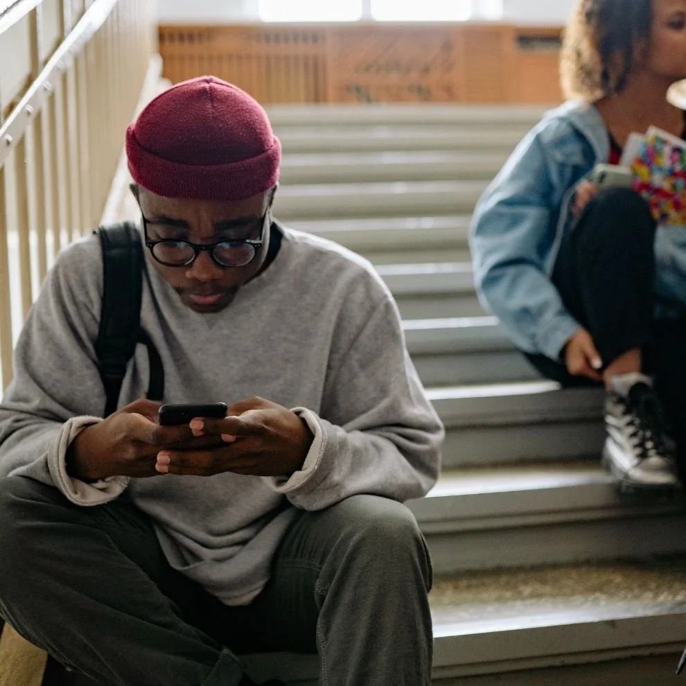 Young person sitting alone on stairs looking at phone showing social isolation.