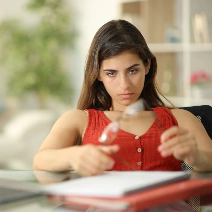 Woman holding eyeglasses looking distracted.