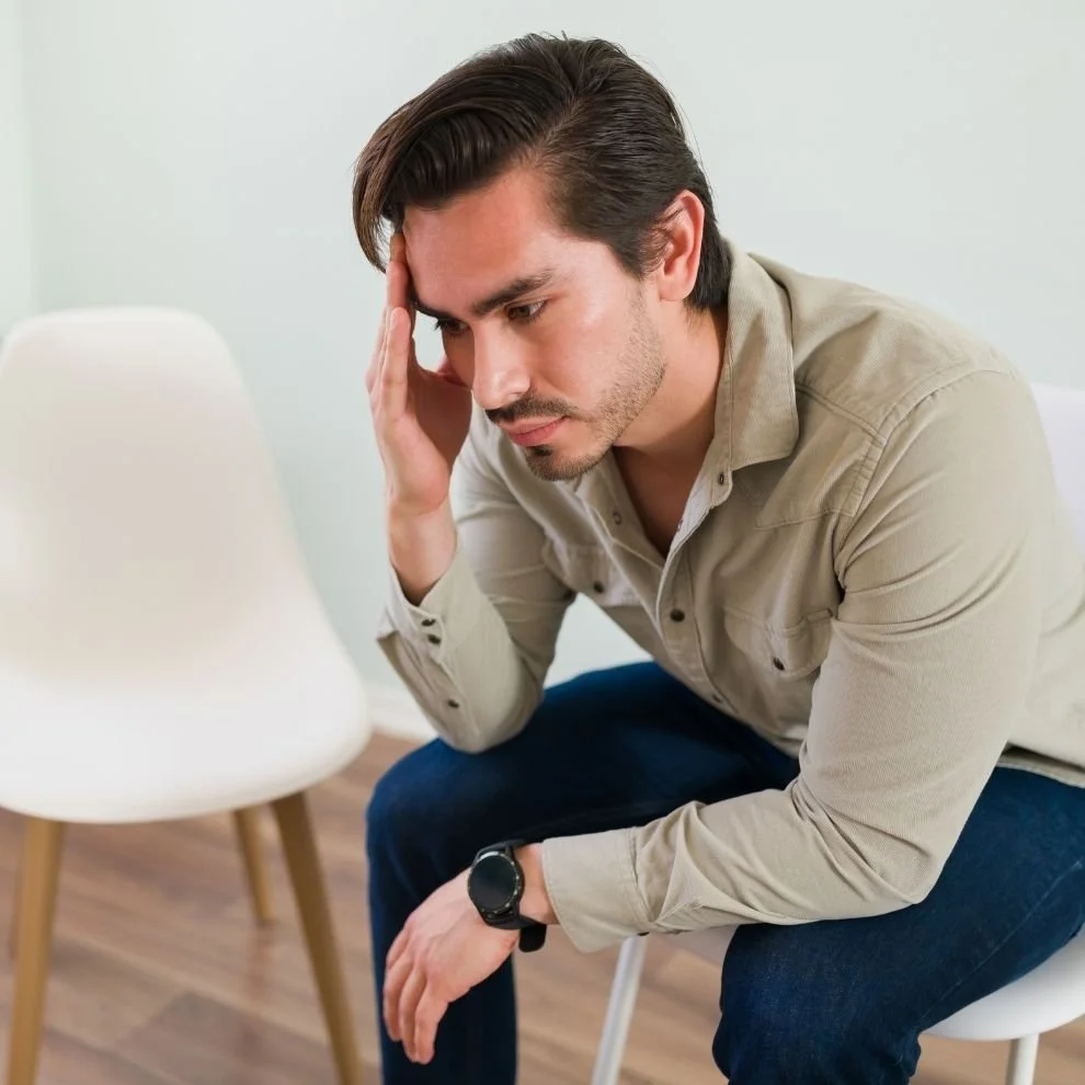 Man sitting with hand on forehead, appearing stressed and mentally overwhelmed.