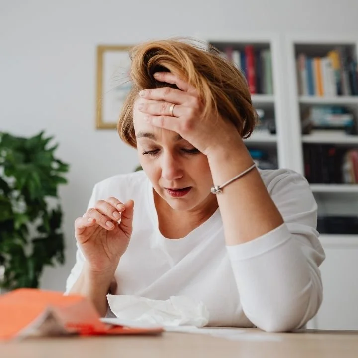 Woman holding her head while sitting at table feeling overwhelmed.