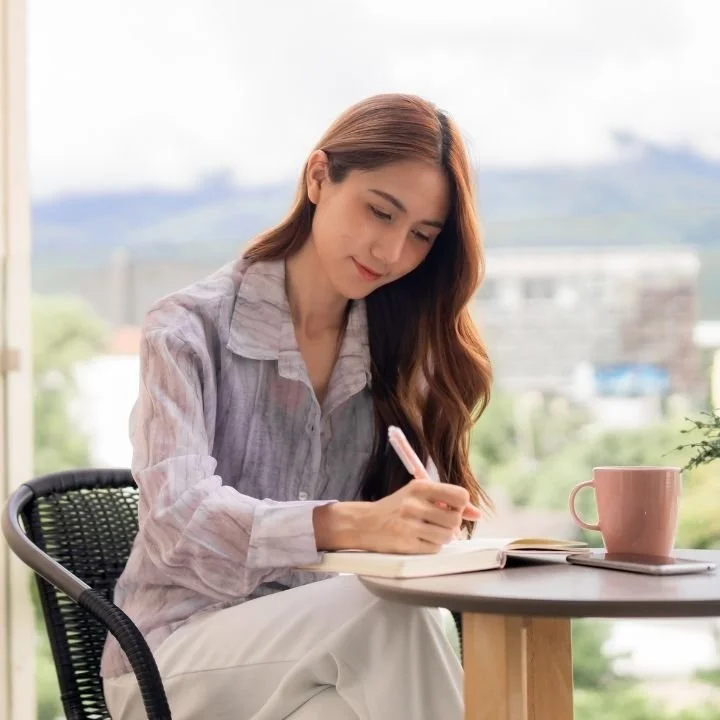 Woman leaning forward and writing in a notebook with a focused expression.
