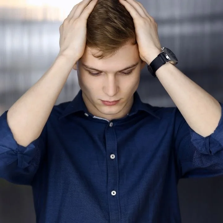 Young man holding head with hands, appearing mentally overwhelmed.