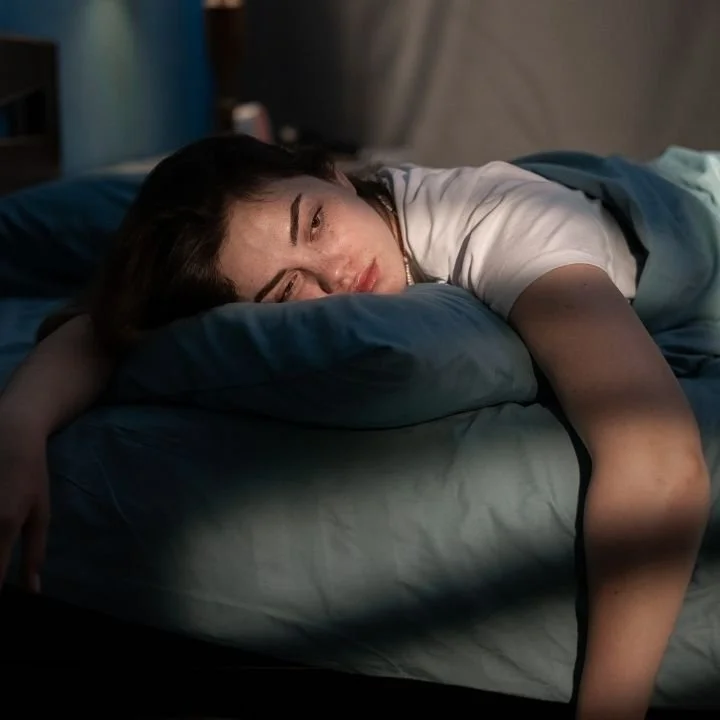 Woman lying in bed at night with tired expression.