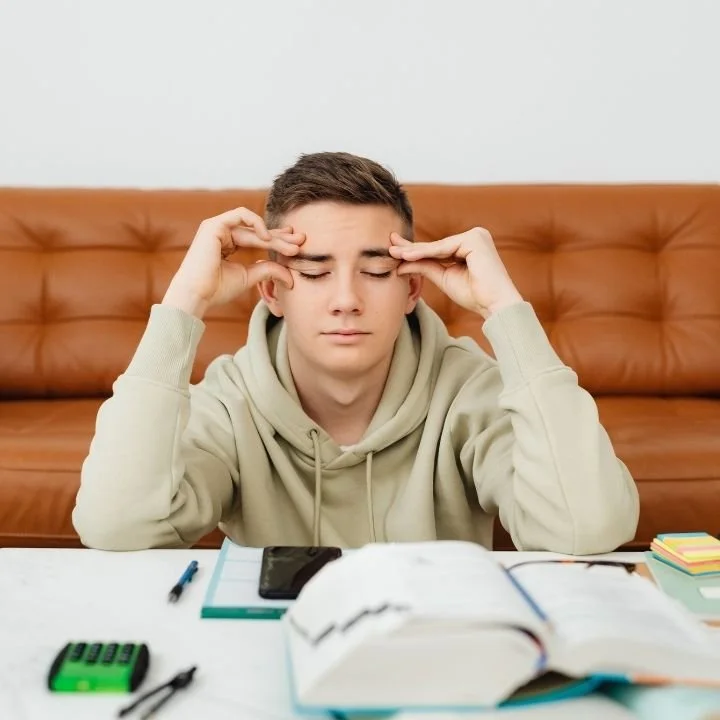 Teen boy sitting at desk rubbing temples with eyes closed