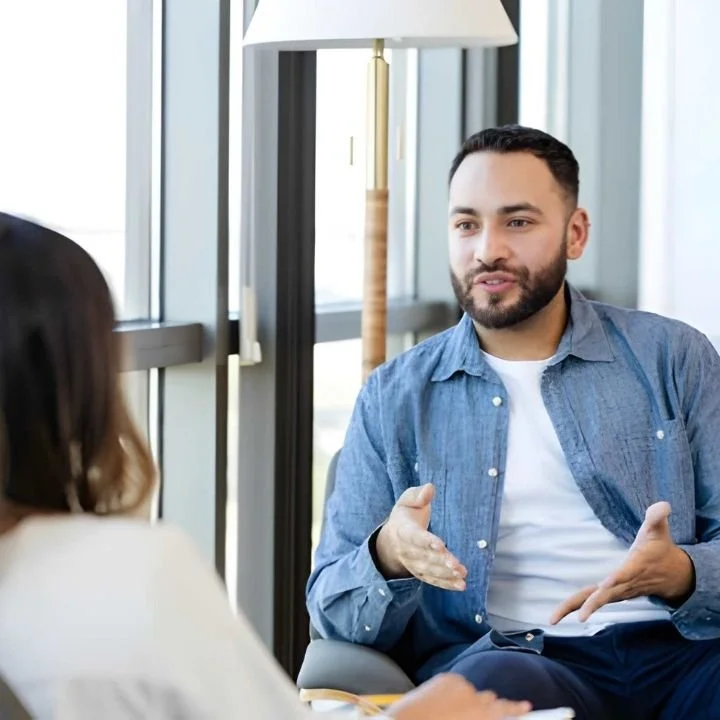 Man gesturing with his hands while speaking to a therapist during a seated therapy session.
