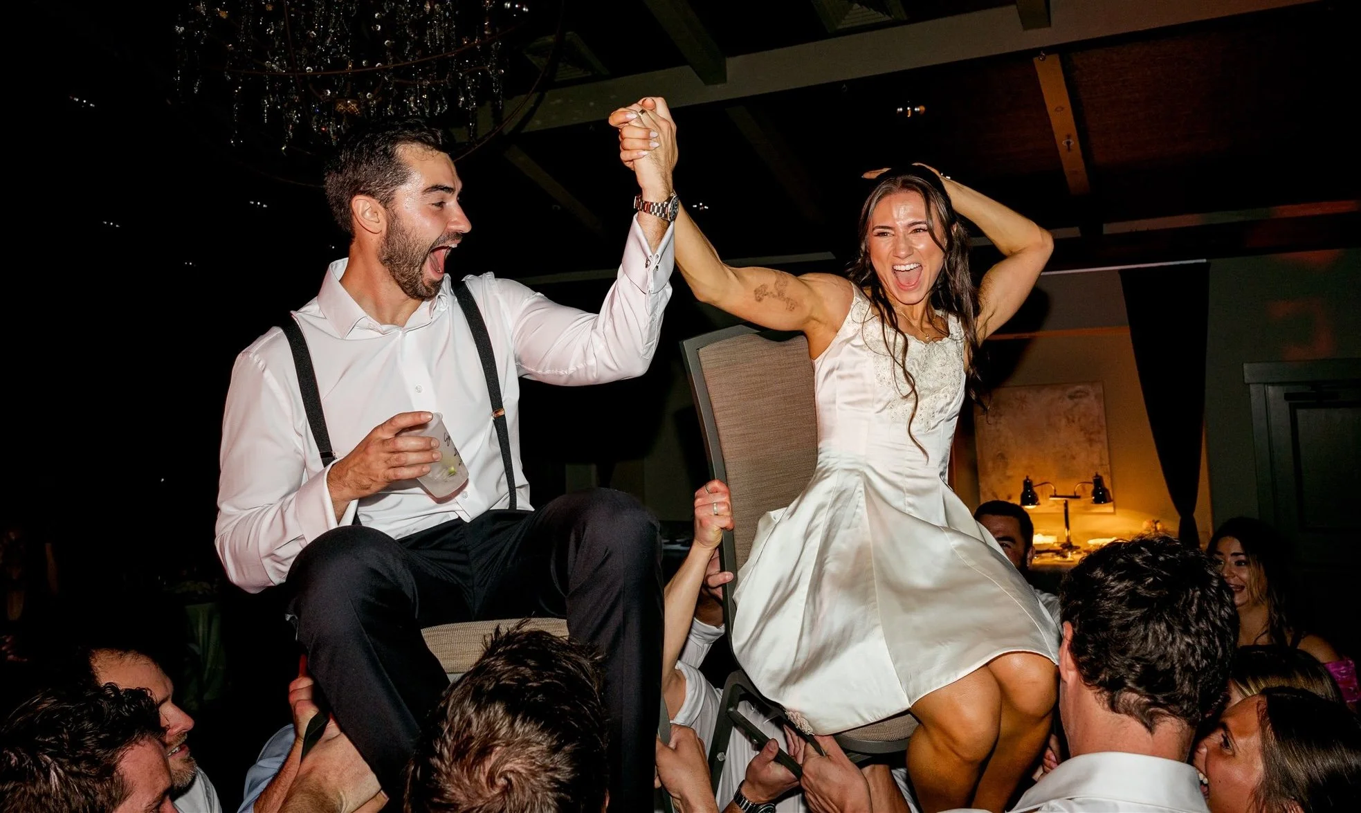 bride and groom being lifted on chairs during a lively wedding celebration.